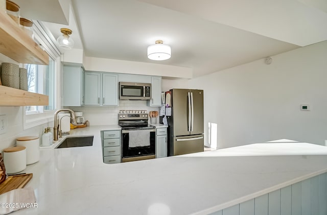 kitchen featuring light stone countertops, a peninsula, a sink, appliances with stainless steel finishes, and backsplash