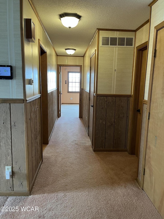 hall featuring ornamental molding, light colored carpet, a textured ceiling, and wood walls