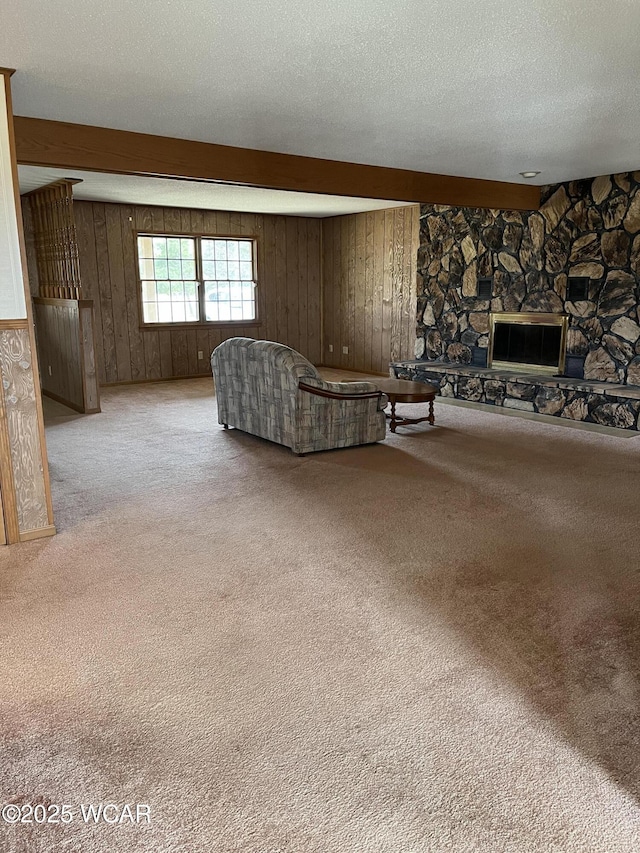 unfurnished living room with light carpet, a stone fireplace, a textured ceiling, and wood walls