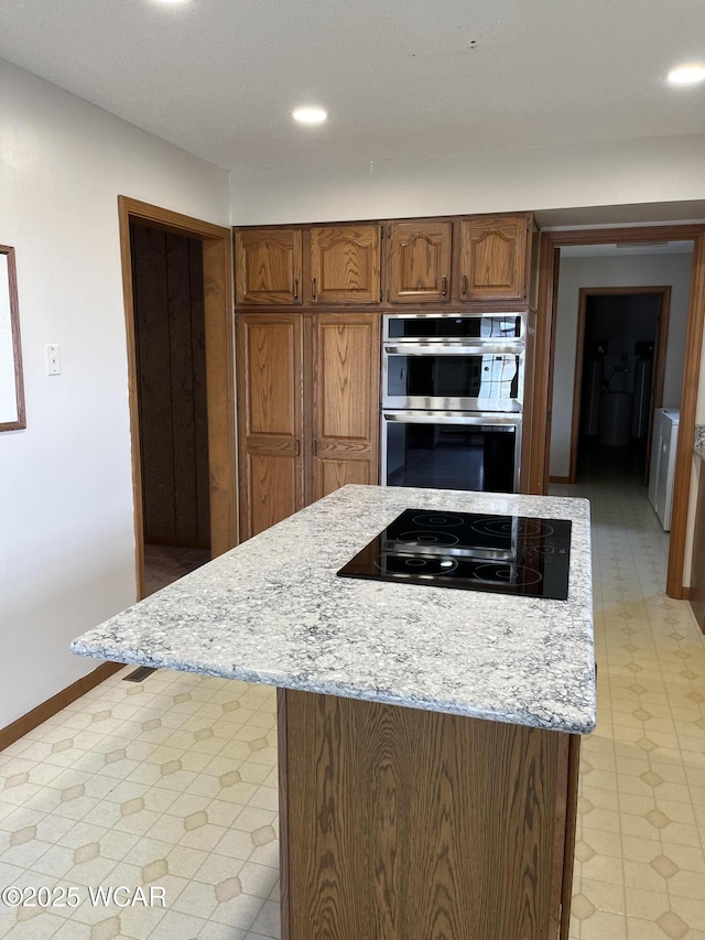 kitchen featuring black electric cooktop, light stone counters, stainless steel double oven, and a kitchen island