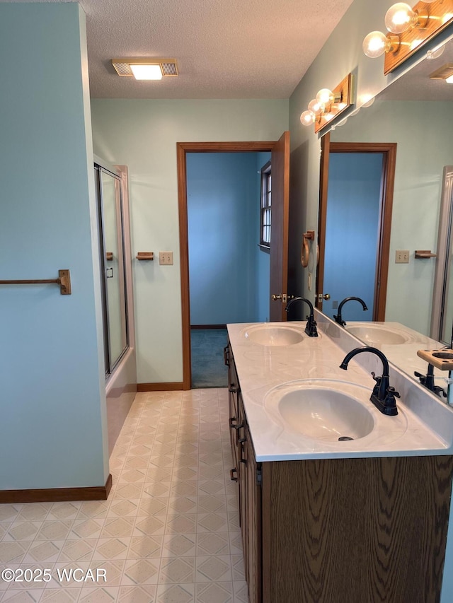 bathroom with vanity, a textured ceiling, and combined bath / shower with glass door