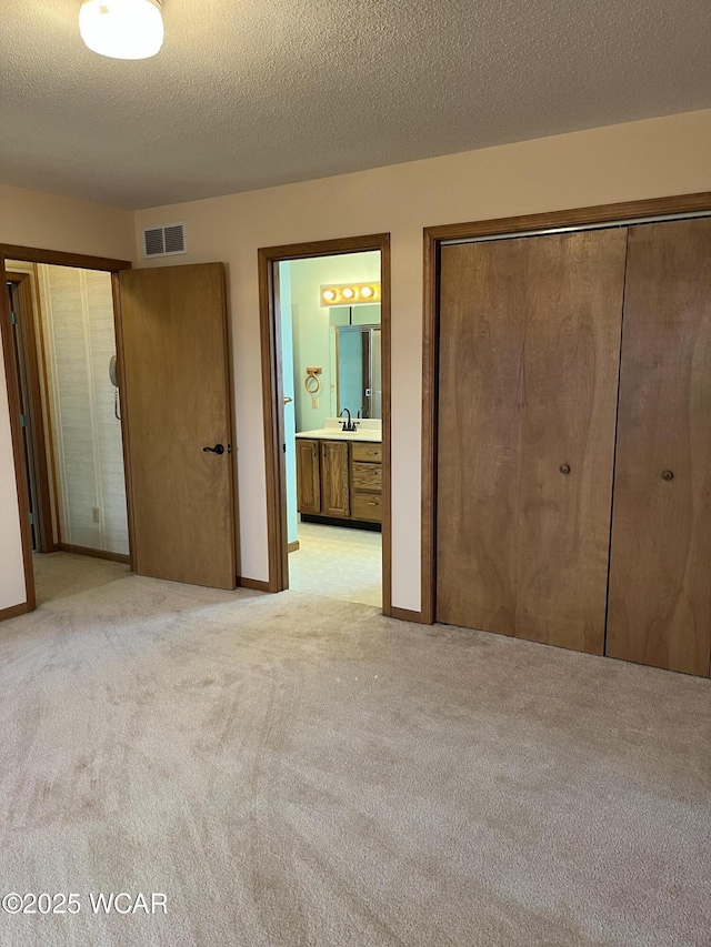 unfurnished bedroom with light colored carpet, connected bathroom, sink, and a textured ceiling