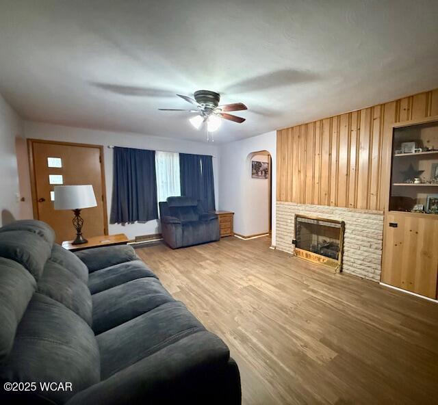 living room featuring light wood-type flooring, built in shelves, a fireplace, and a ceiling fan