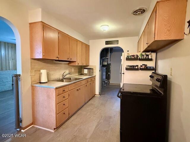 kitchen with a sink, arched walkways, light countertops, and black range with electric stovetop