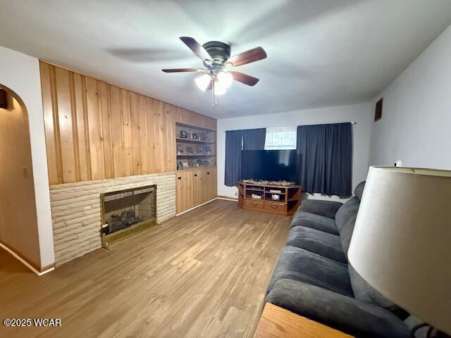 living room featuring arched walkways, ceiling fan, a fireplace, wood finished floors, and built in features