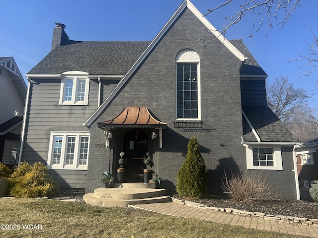 view of front facade featuring brick siding, roof with shingles, and a chimney