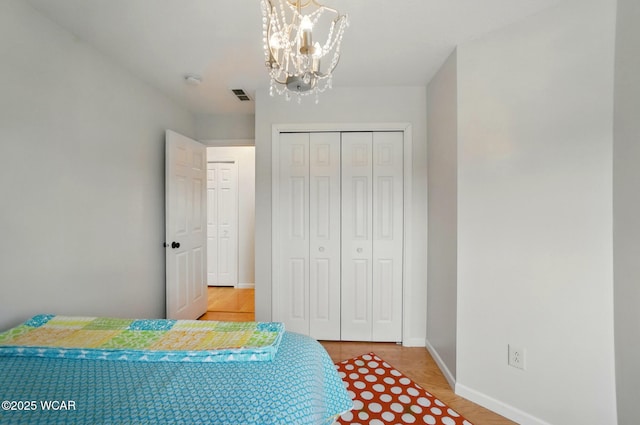 bedroom with visible vents, baseboards, a closet, a chandelier, and light wood-style floors