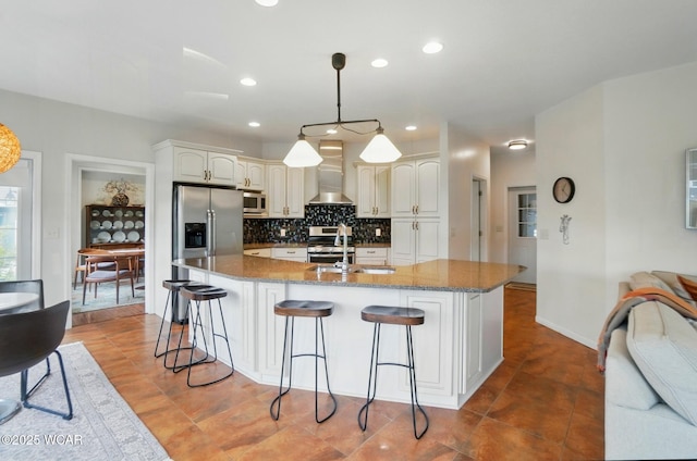 kitchen with decorative backsplash, a kitchen bar, wall chimney exhaust hood, a sink, and stainless steel appliances