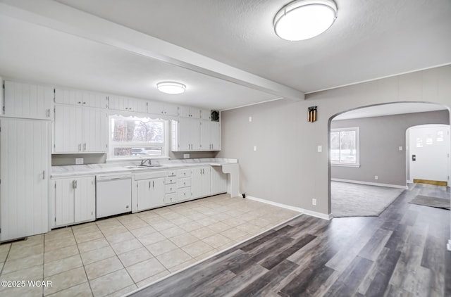 kitchen with sink, light hardwood / wood-style flooring, dishwasher, white cabinets, and beamed ceiling