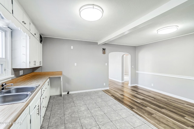 kitchen with sink, light tile patterned floors, beamed ceiling, and white cabinets