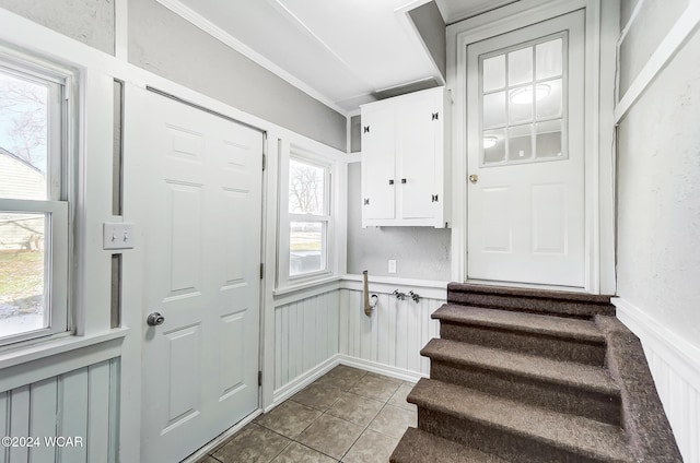 entryway featuring crown molding, a healthy amount of sunlight, light tile patterned floors, and electric panel