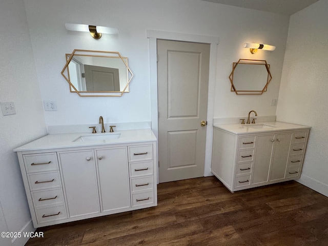 full bath featuring two vanities, wood finished floors, baseboards, and a sink