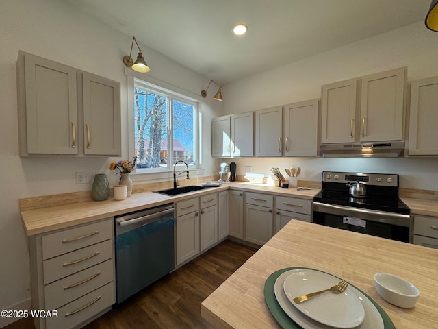 kitchen with gray cabinets, under cabinet range hood, a sink, dark wood finished floors, and appliances with stainless steel finishes