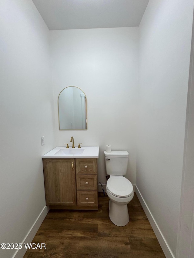 half bath with baseboards, toilet, wood finished floors, and vanity