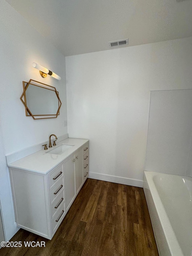 bathroom featuring visible vents, wood finished floors, baseboards, a bath, and vanity