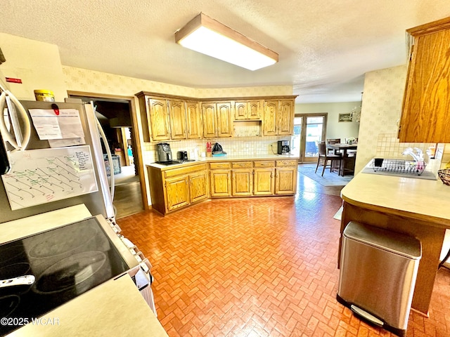 2969 Sands Rd, Lima, OH 45805 - kitchen with brick patterned floors, light countertops, backsplash, electric range, and wallpapered walls