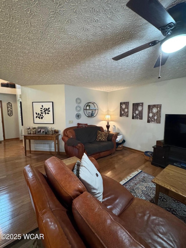 living room with ceiling fan, a textured ceiling, hardwood / wood-style flooring, and baseboards