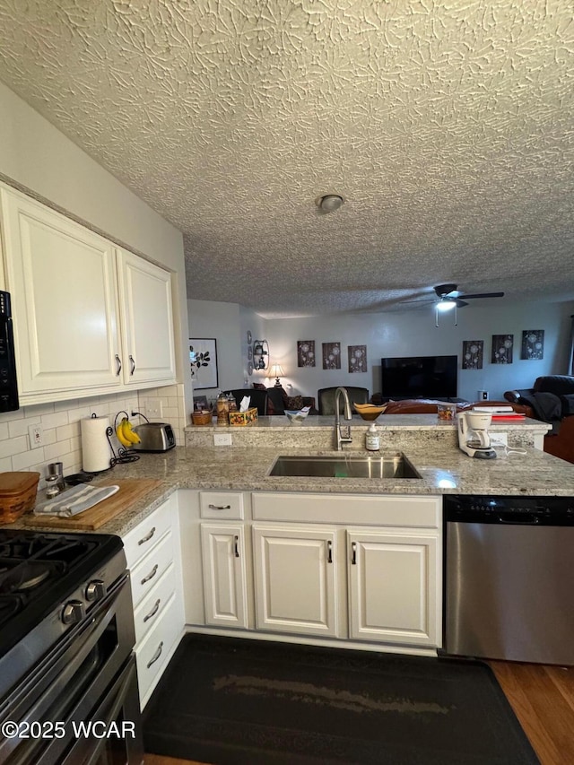 kitchen with open floor plan, white cabinetry, ceiling fan, stainless steel appliances, and a sink