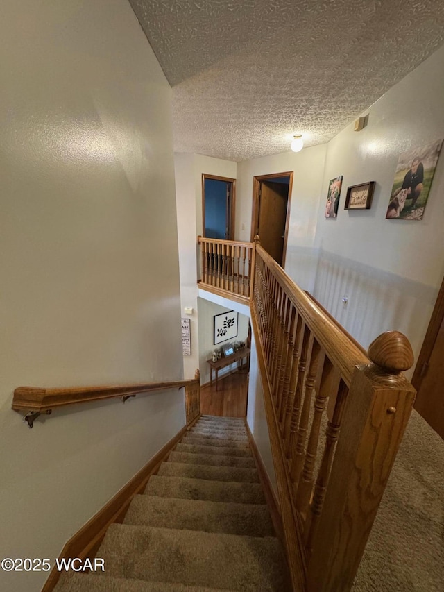 stairway with carpet and a textured ceiling