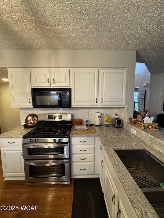 kitchen with dark wood-style flooring, black microwave, backsplash, white cabinets, and double oven range