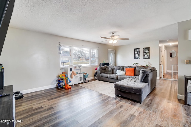 living room with a textured ceiling, wood finished floors, a ceiling fan, and baseboards