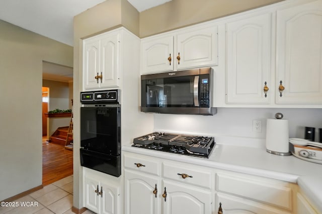 kitchen with black appliances, a warming drawer, light tile patterned floors, and white cabinets