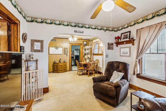 sitting room featuring arched walkways, baseboards, ceiling fan, and carpet