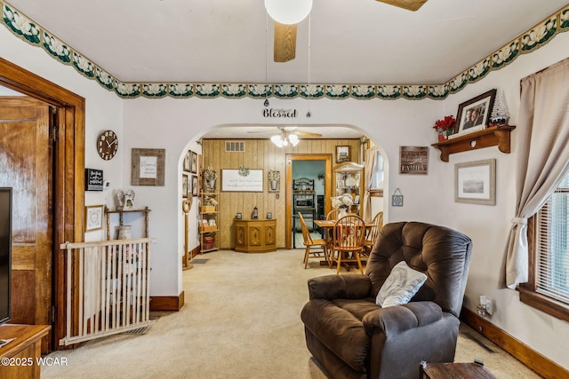 carpeted living room with baseboards, visible vents, arched walkways, and a ceiling fan