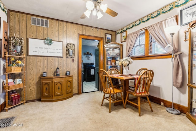 dining space with a ceiling fan, carpet, visible vents, and wooden walls