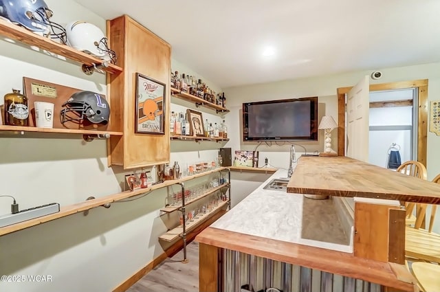 bar with baseboards, a sink, and light wood-style floors