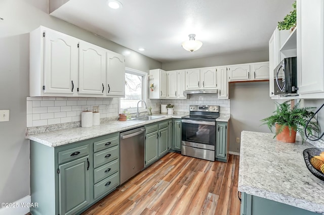 kitchen featuring white cabinets, light wood-style floors, appliances with stainless steel finishes, under cabinet range hood, and a sink