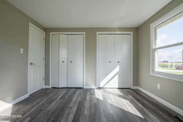 unfurnished bedroom with multiple closets and dark hardwood / wood-style floors