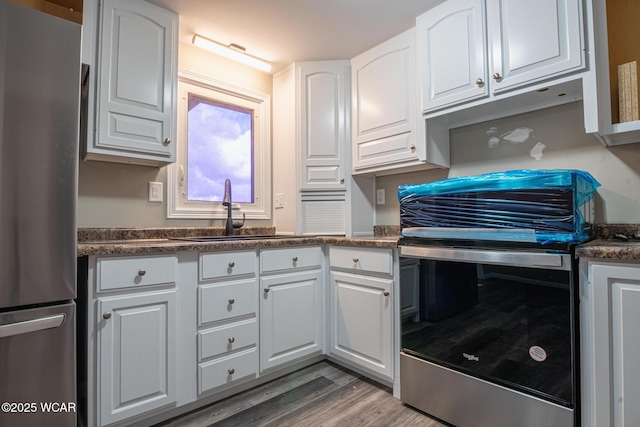 kitchen with sink, wood-type flooring, white cabinets, and appliances with stainless steel finishes