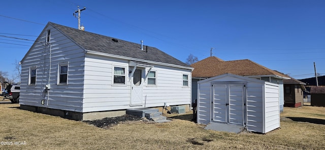 rear view of house featuring central AC, a shingled roof, an outdoor structure, a yard, and a shed