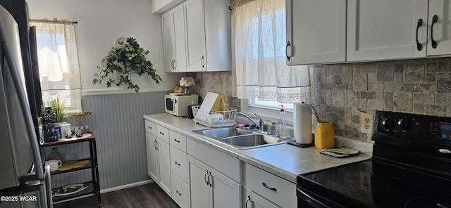 kitchen featuring electric range, freestanding refrigerator, wainscoting, white cabinets, and a sink