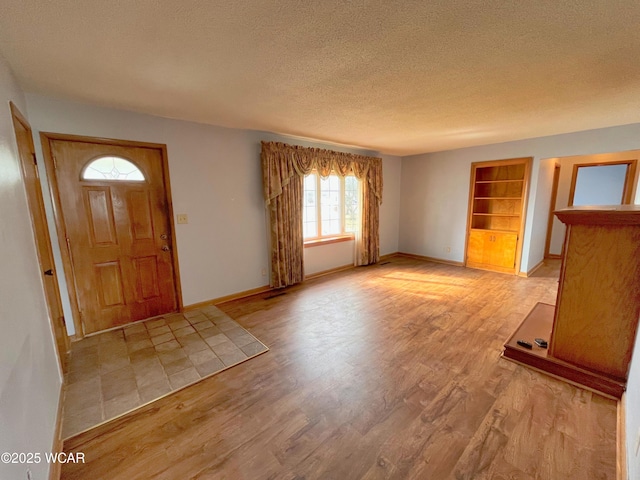 foyer entrance featuring light wood finished floors, baseboards, and a textured ceiling