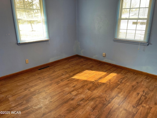 empty room with plenty of natural light, visible vents, and wood finished floors