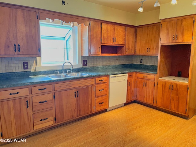 kitchen featuring light wood-style floors, dark countertops, white dishwasher, and a sink