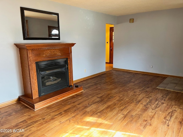 unfurnished living room with a fireplace with raised hearth, wood finished floors, and baseboards