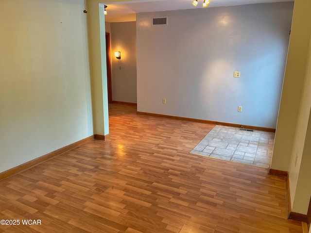 spare room with wood finished floors, visible vents, and baseboards