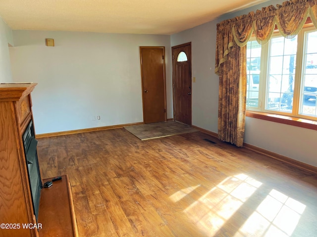 foyer entrance featuring visible vents, a fireplace, baseboards, and wood finished floors