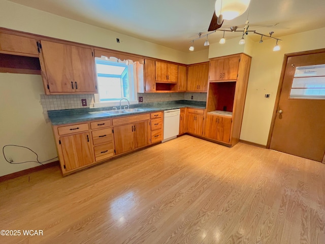 kitchen with light wood finished floors, tasteful backsplash, dark countertops, white dishwasher, and a sink