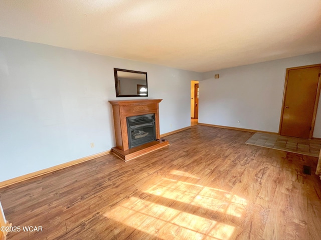 unfurnished living room featuring light wood-style floors, a glass covered fireplace, and baseboards