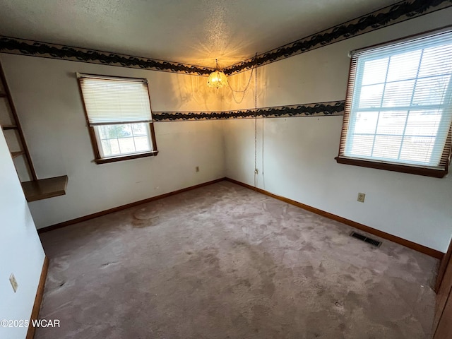 empty room with baseboards, visible vents, light colored carpet, a textured ceiling, and a chandelier