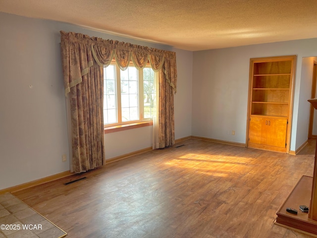 unfurnished living room featuring a textured ceiling, wood finished floors, and baseboards