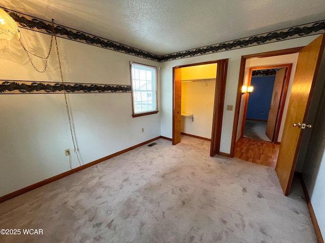 unfurnished bedroom featuring a textured ceiling, light colored carpet, visible vents, baseboards, and a closet