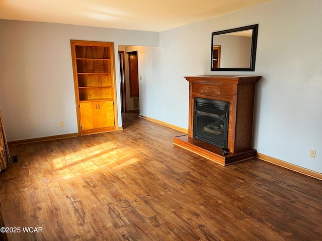 unfurnished living room with a fireplace with raised hearth, wood finished floors, built in features, and baseboards