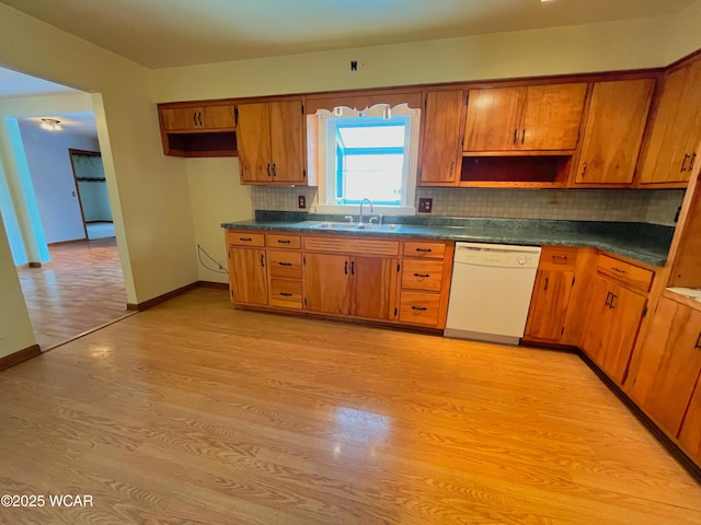 kitchen featuring brown cabinetry, dishwasher, dark countertops, light wood-style floors, and a sink