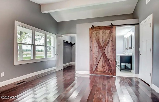 unfurnished bedroom with lofted ceiling with beams, a barn door, and dark hardwood / wood-style floors