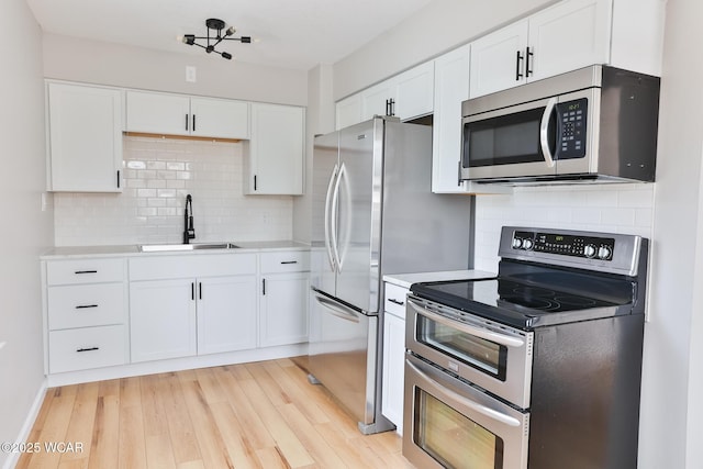 kitchen with stainless steel appliances, light countertops, white cabinets, a sink, and light wood-type flooring